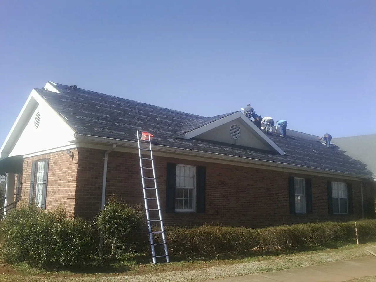 Crew tearing shingles off a brick ranch roof with a ladder set — Metal Roof Repair work by our crew in Wrens