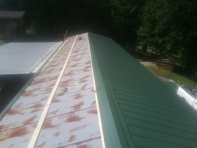 Old rusted panels beside newly installed green metal roofing — Wind Damage Roof Repair by Roofing Brothers in Wrens