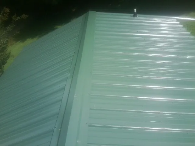 New green metal panels meeting at the ridge of a roof — Flat Roof Repair work by our crew in Wrens