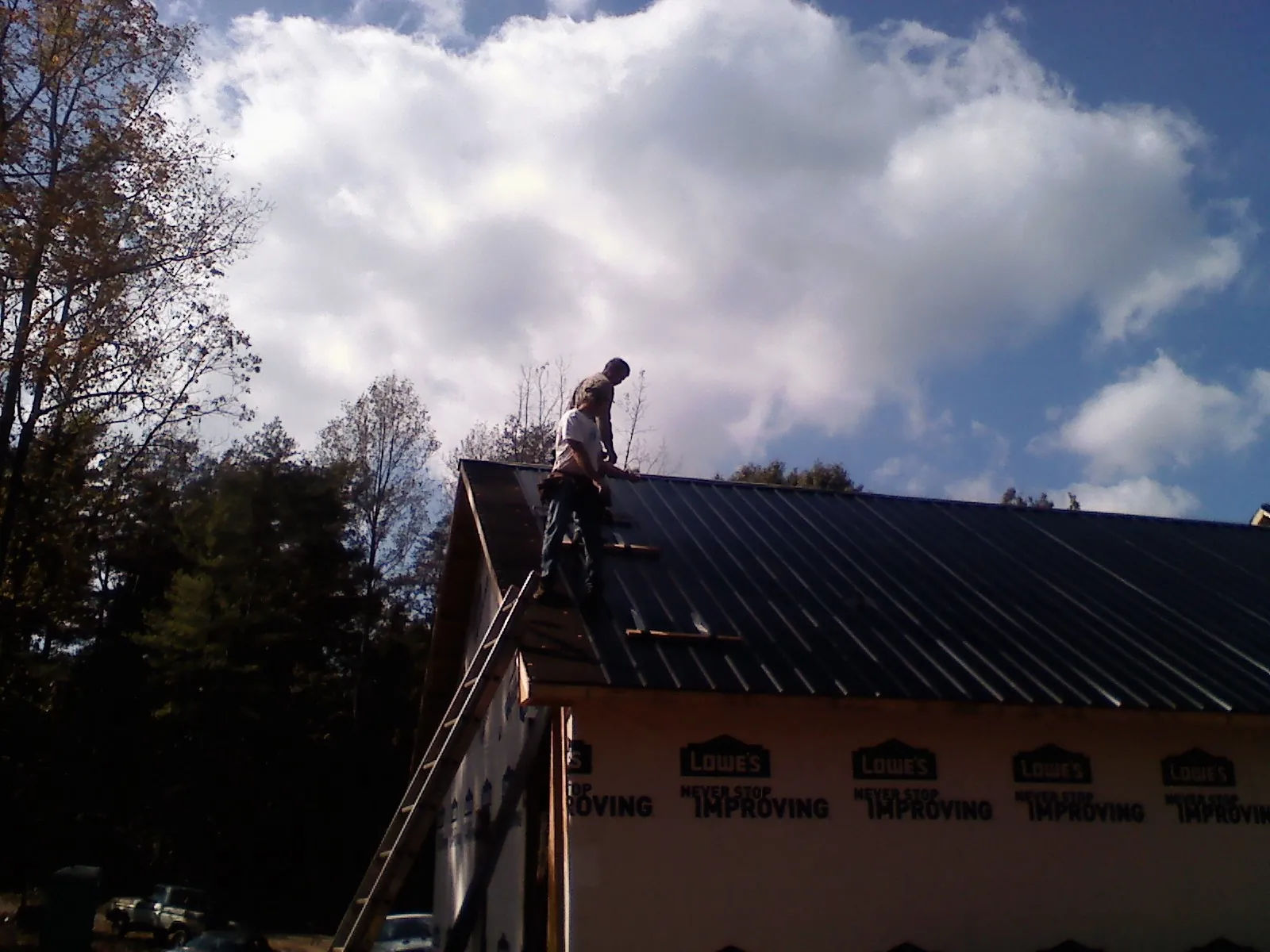Roofer fastening dark metal panels high against a cloudy sky, from a Roof Inspection job in Wrens