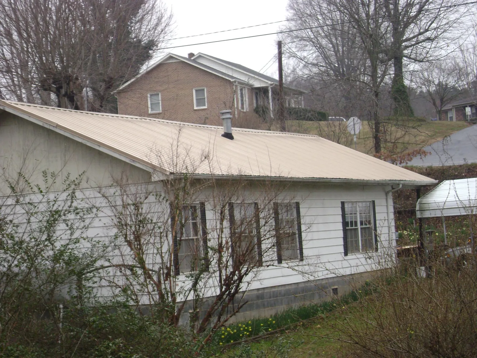 Tan metal roof on a white sided house set into a hillside — Commercial Roofing by Roofing Brothers in Wrens